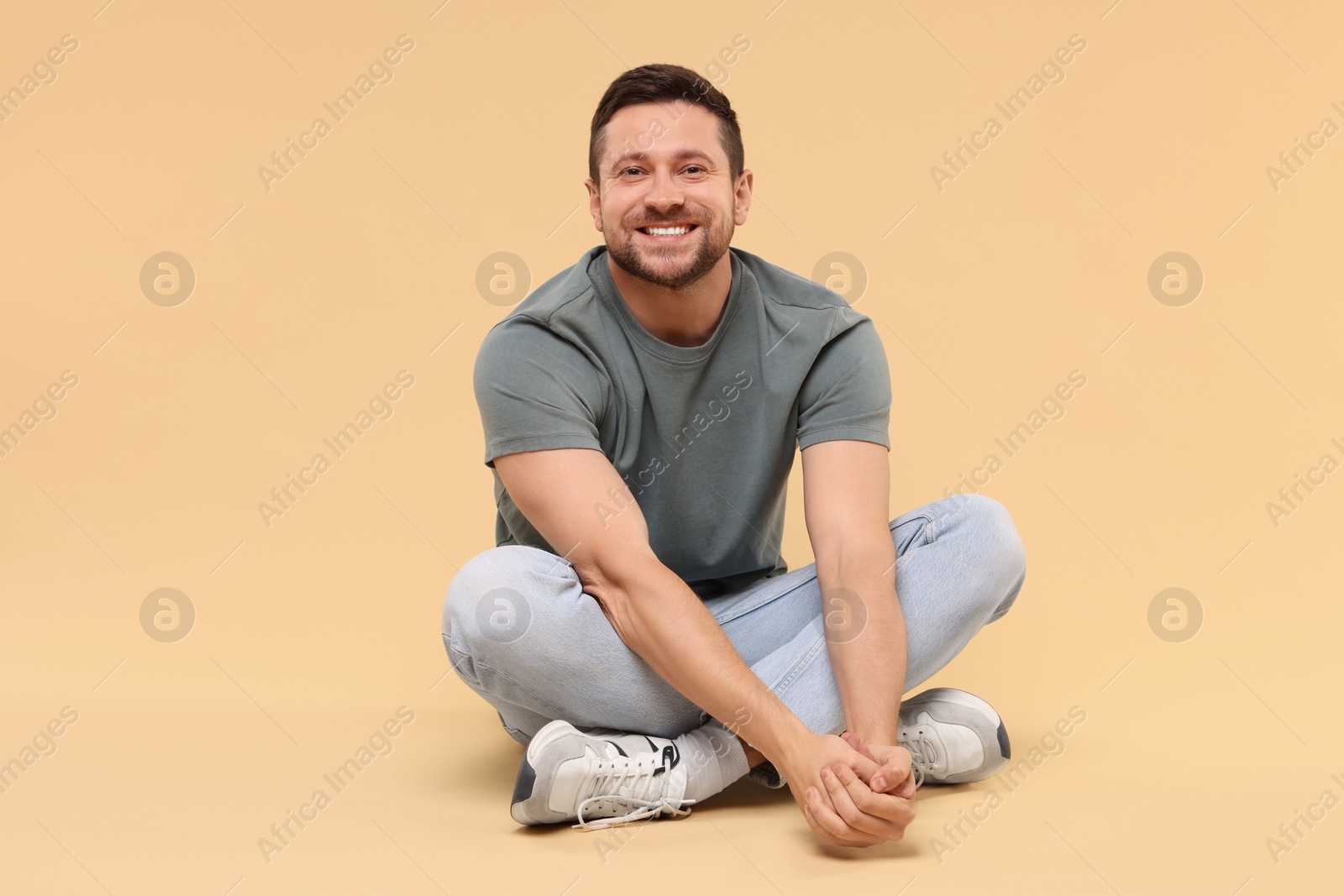 Photo of Happy handsome man sitting on beige background