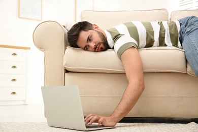 Lazy young man using laptop while lying on sofa at home