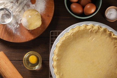 Photo of Pie tin with fresh dough and ingredients on wooden table, flat lay. Making quiche