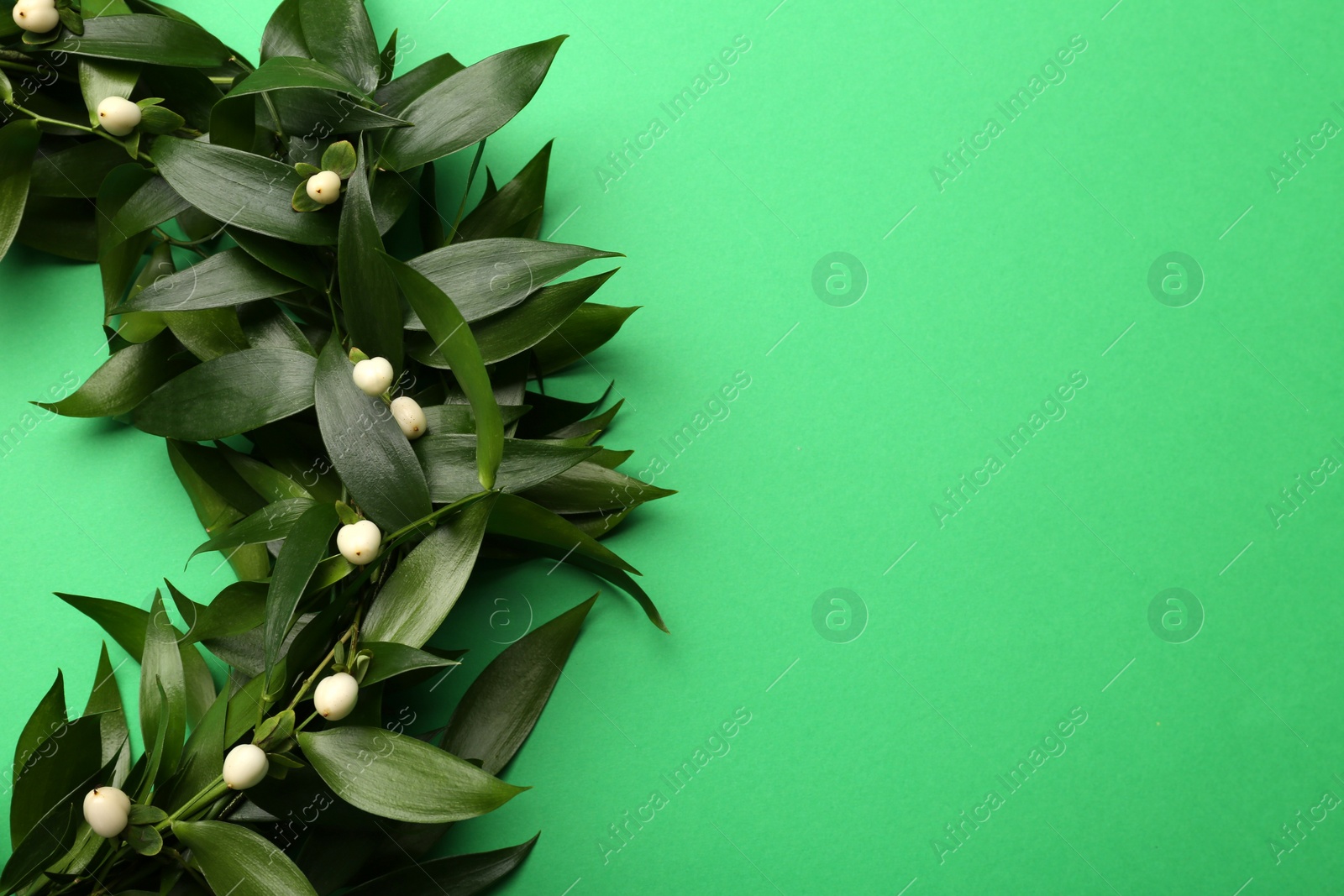 Photo of Beautiful handmade mistletoe wreath on green background, top view. Space for text