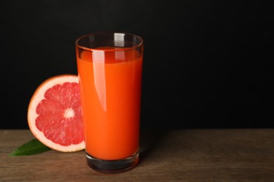 Photo of Tasty grapefruit juice in glass, leaf and fresh fruit on wooden table against black background. Space for text