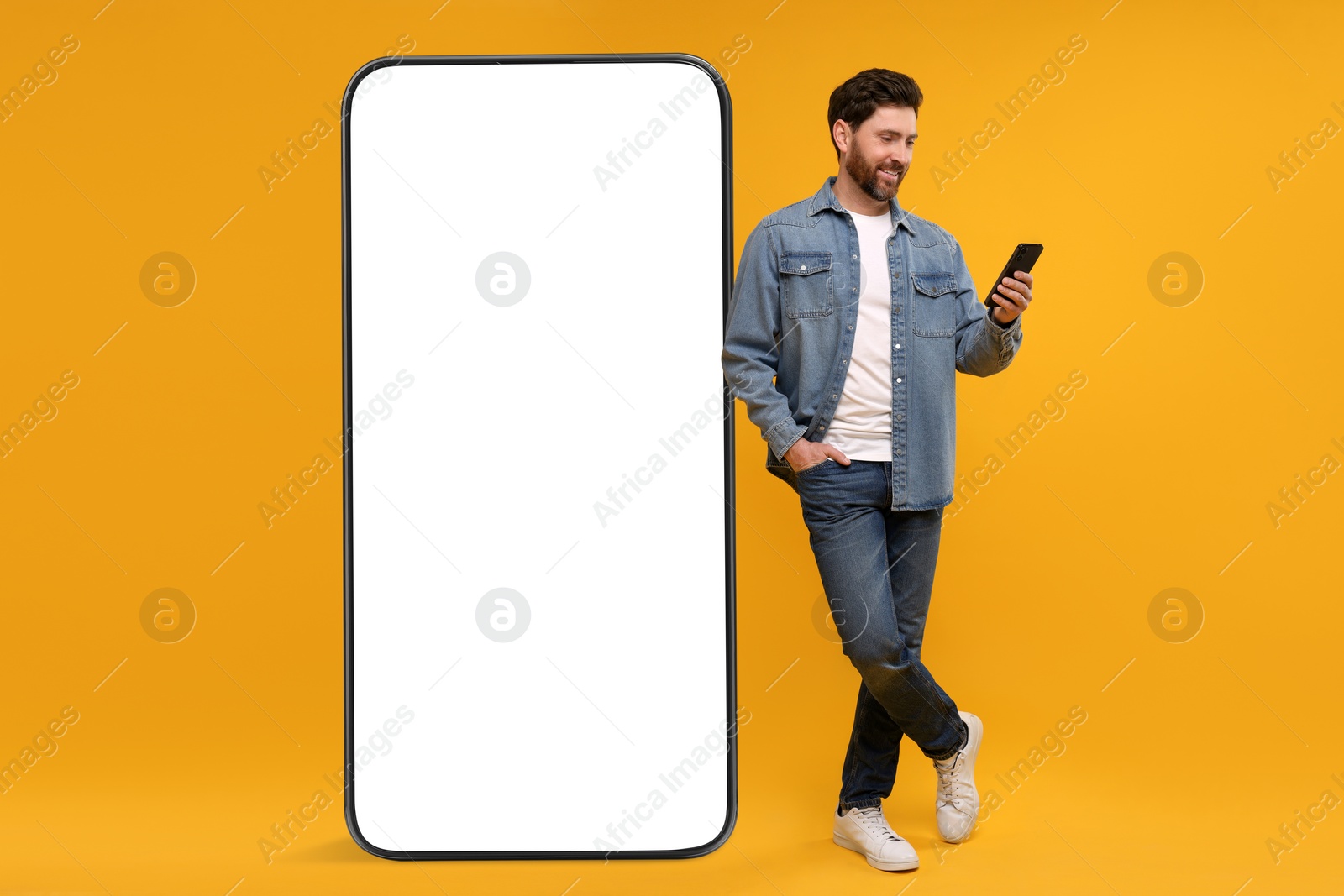 Image of Man with mobile phone standing near huge device with empty screen on orange background. Mockup for design