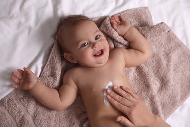 Photo of Mother applying moisturizing cream onto her little baby's skin on towel, closeup