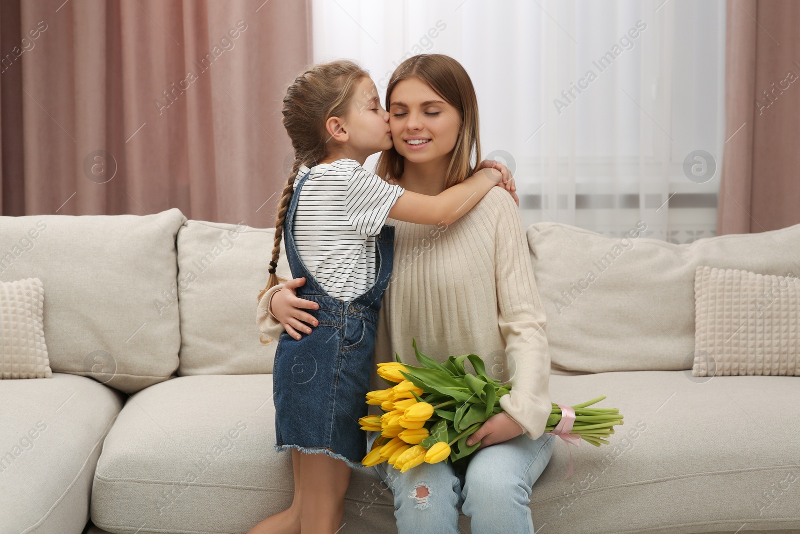 Photo of Little daughter congratulating mom with bouquet of yellow tulips at home. Happy Mother's Day