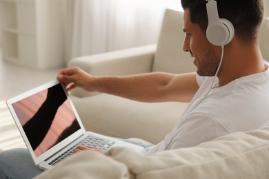 Man with laptop and headphones sitting on sofa at home