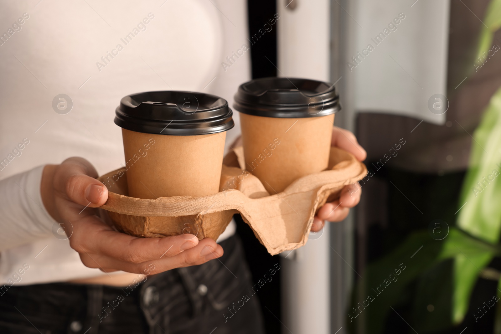 Photo of Woman holding paper coffee cups indoors, closeup