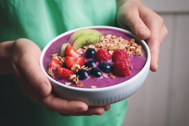 Woman holding bowl with tasty acai smoothie and fruits on blurred background, closeup