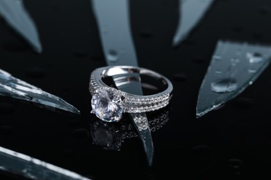 Photo of Luxury jewelry. Stylish presentation of elegant ring on black mirror surface with broken glass, closeup