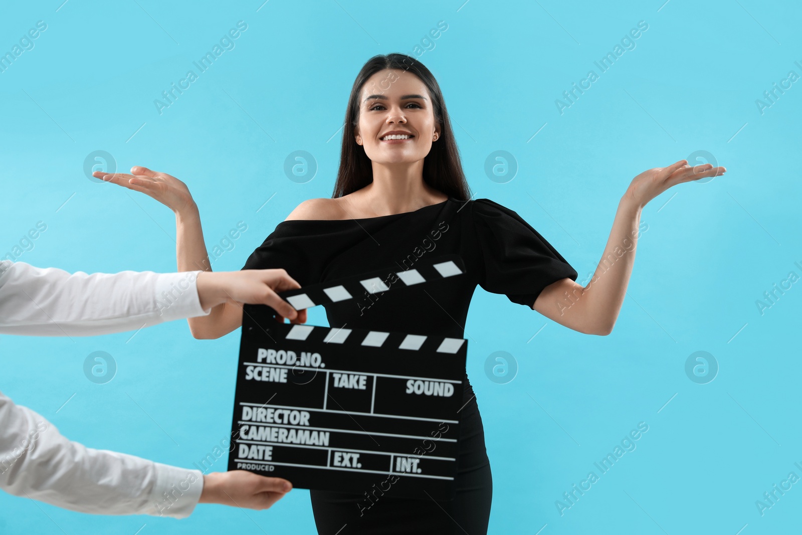 Photo of Happy actress performing while second assistant camera holding clapperboard on light blue background. Film industry