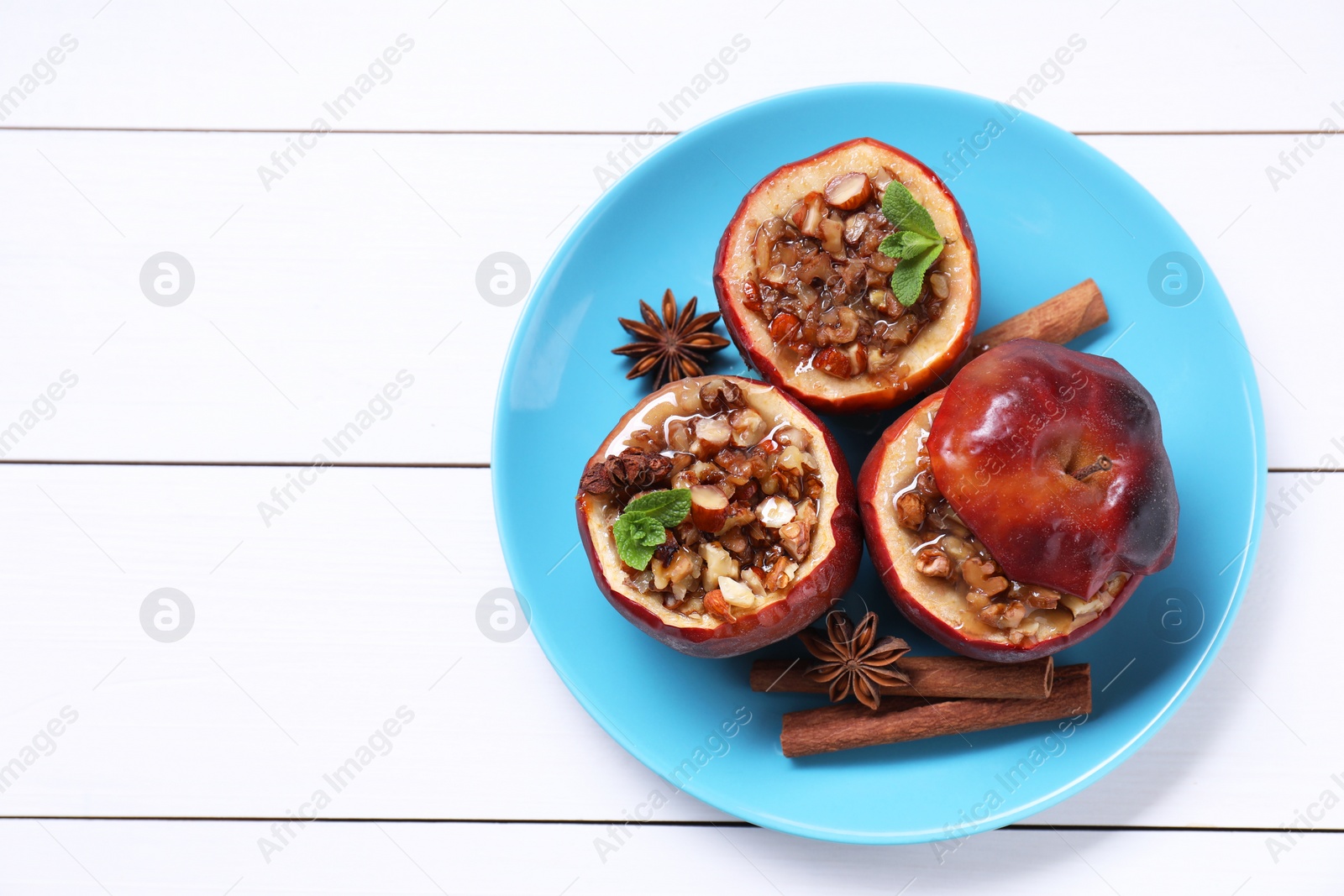 Photo of Tasty baked apples with nuts, honey, spices and mint on white wooden table, top view. Space for text