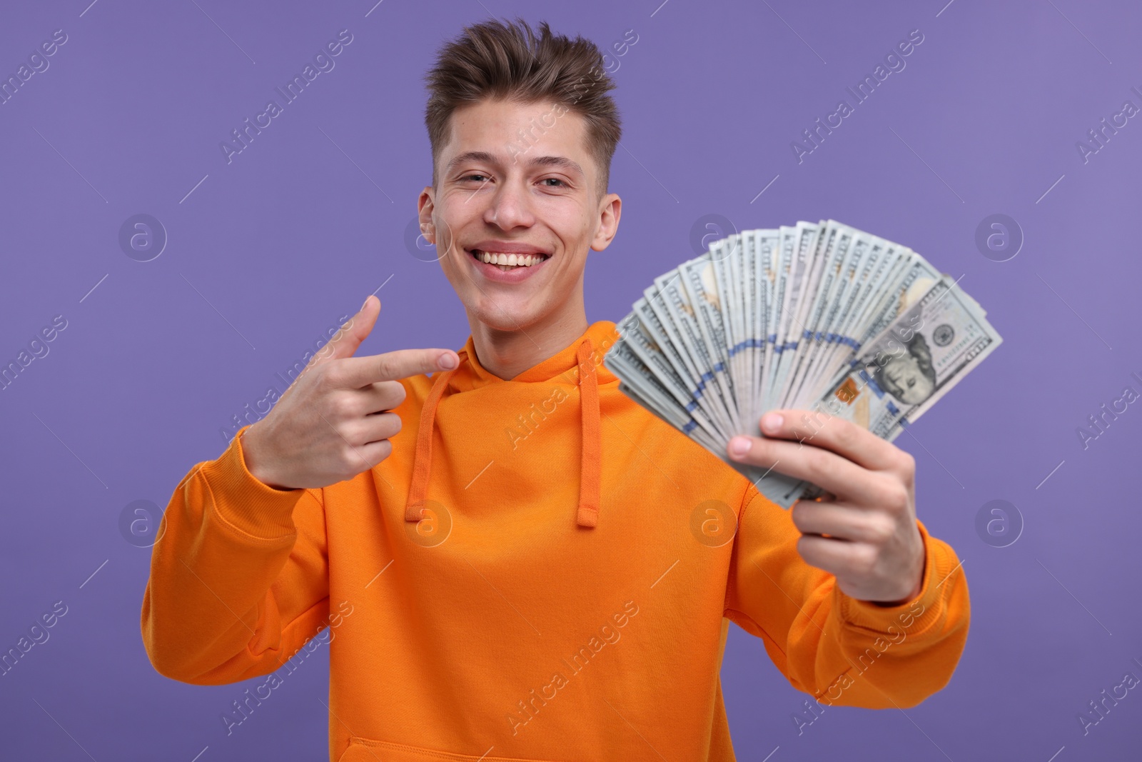 Photo of Happy man pointing at money on purple background, selective focus