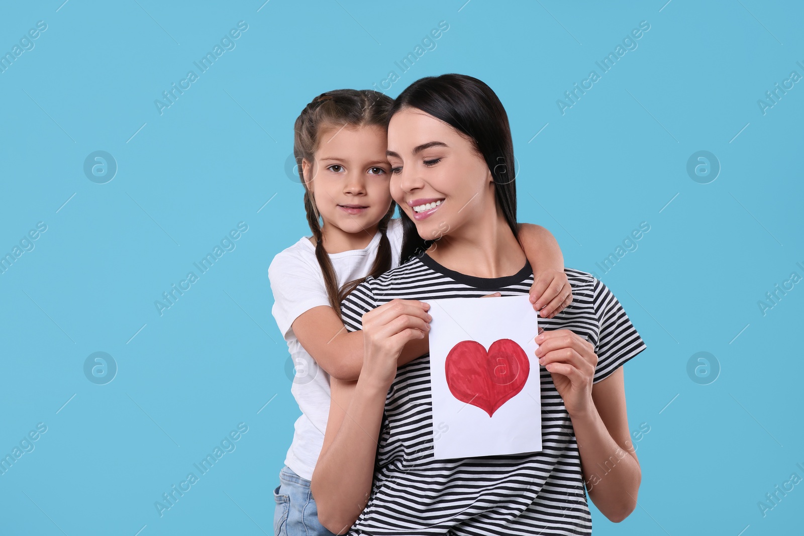 Photo of Happy woman with her cute daughter and handmade greeting card on light blue background. Mother's day celebration