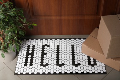 Photo of Stylish door mat with word HELLO, cardboard boxes and houseplant on floor