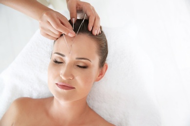 Photo of Young woman undergoing acupuncture treatment in salon