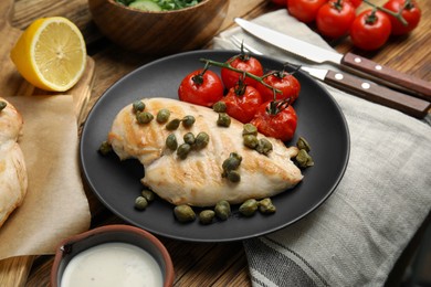 Photo of Delicious cooked chicken fillet with capers and tomatoes served on wooden table