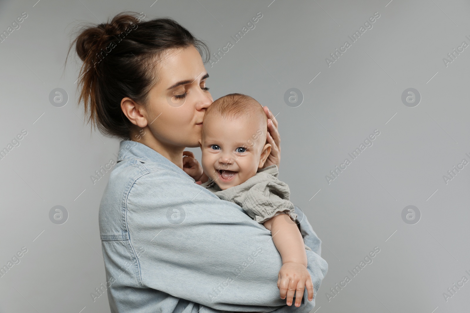 Photo of Beautiful mother kissing her cute baby on grey background. Space for text