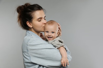 Photo of Beautiful mother kissing her cute baby on grey background. Space for text