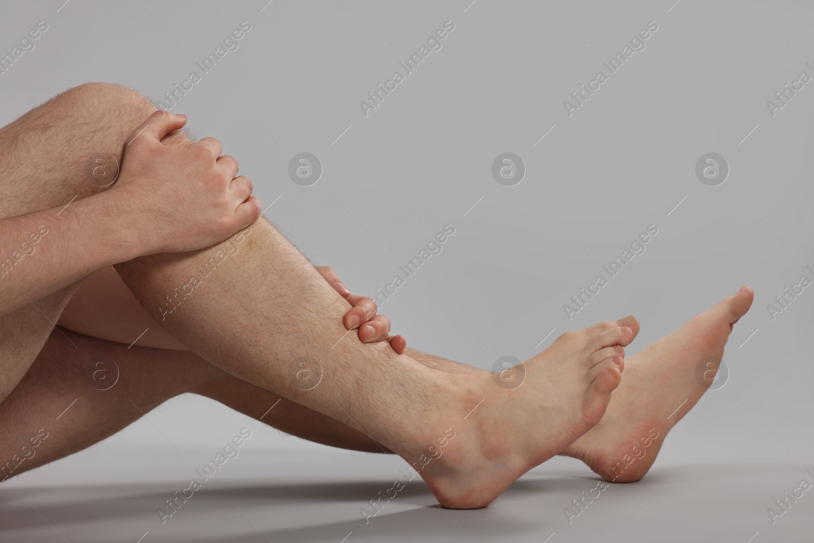 Photo of Man suffering from leg pain on grey background, closeup