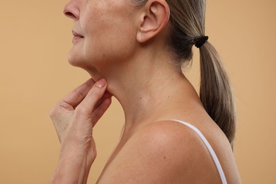 Photo of Mature woman touching her neck on beige background, closeup