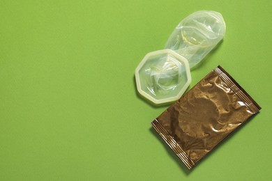 Unrolled female condom and package on green background, above view with space for text. Safe sex
