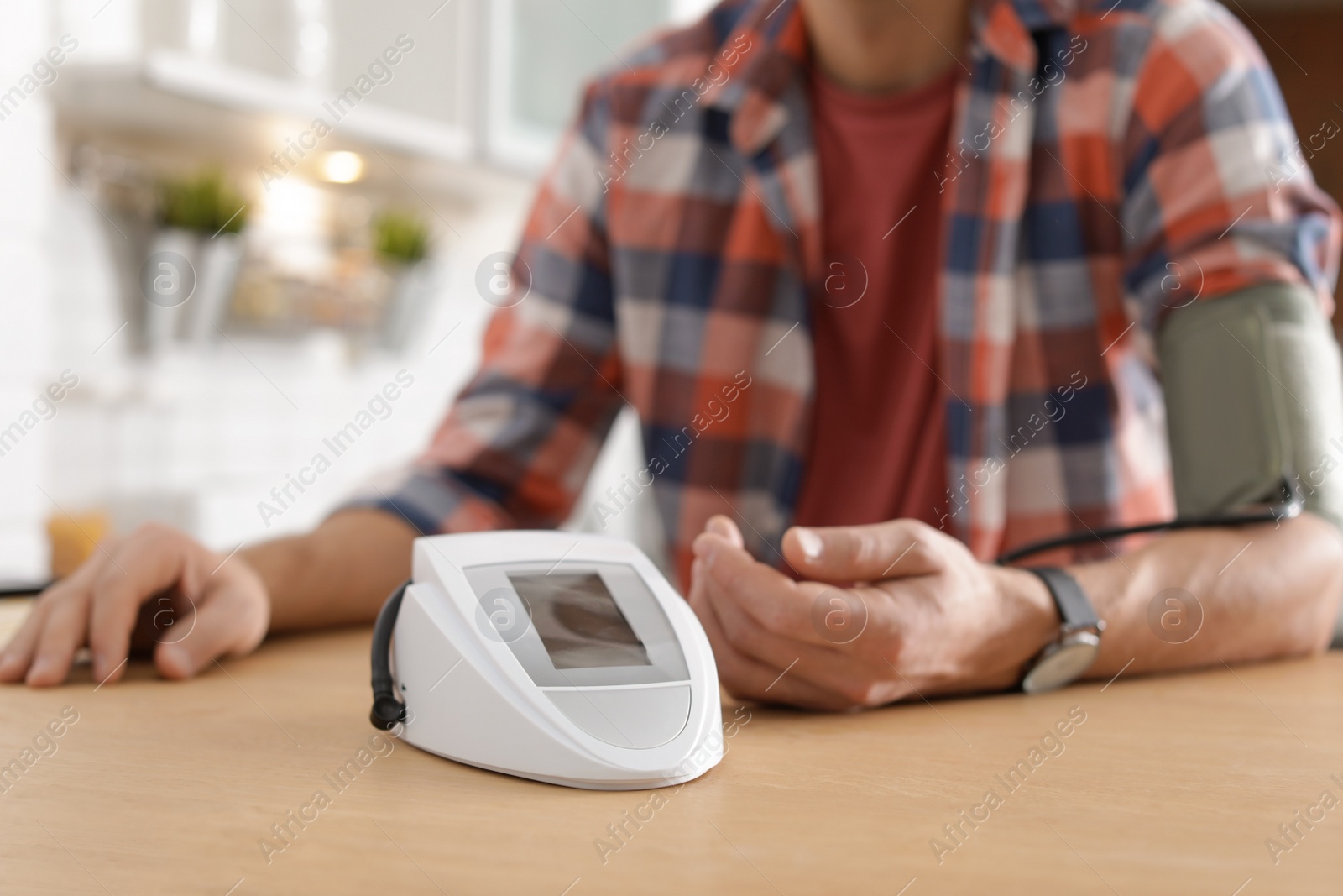 Photo of Man checking blood pressure with sphygmomanometer at table indoors, closeup. Cardiology concept