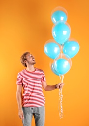 Young man with air balloons on color background