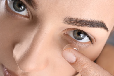 Photo of Young woman putting contact lens in her eye, closeup