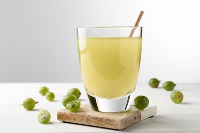 Photo of Tasty gooseberry juice on white wooden table against light background