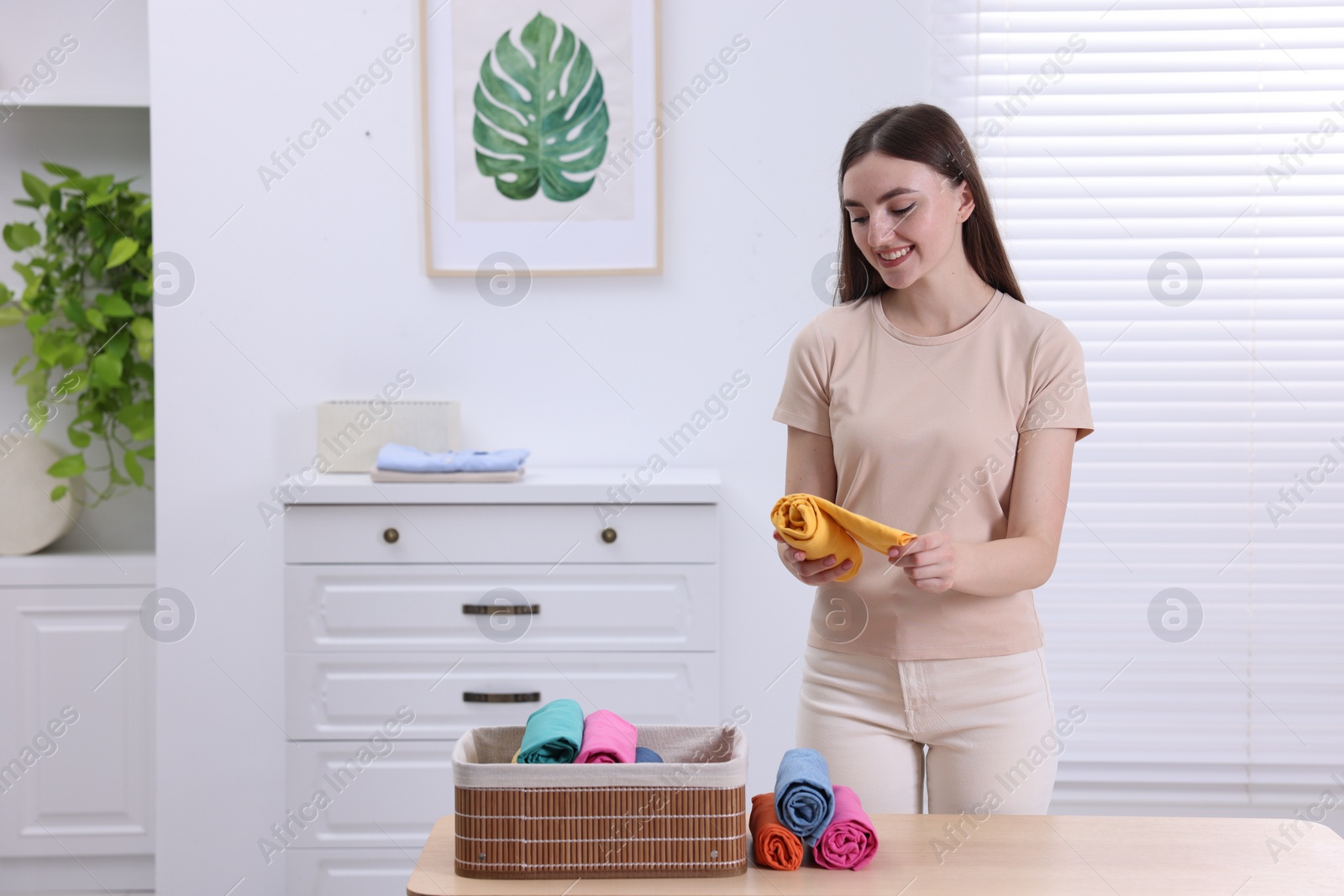 Photo of Young woman rolling shirt in room, space for text. Organizing clothes