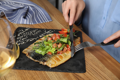 Photo of Woman eating delicious grilled fish with vegetables at wooden table, closeup