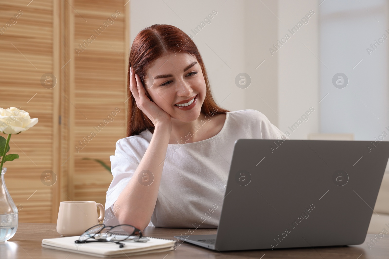 Photo of Happy woman using laptop at wooden table in room