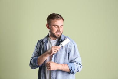 Photo of Young man cleaning clothes with lint roller on light background