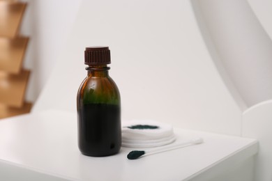 Bottle of brilliant green, cotton bud and pads on white table indoors. Space for text