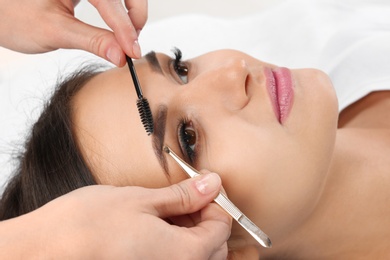 Photo of Young woman having professional eyebrow correction procedure in beauty salon