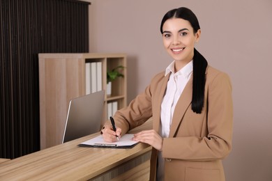 Photo of Receptionist with clipboard near countertop in office