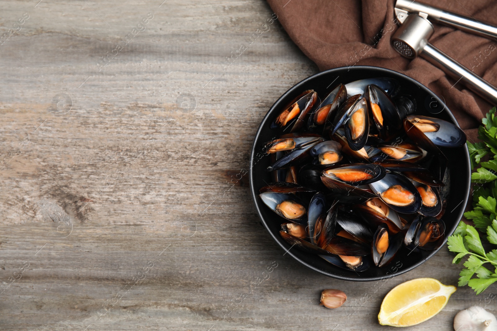 Photo of Bowl of delicious cooked mussels with parsley and lemon on wooden table, flat lay