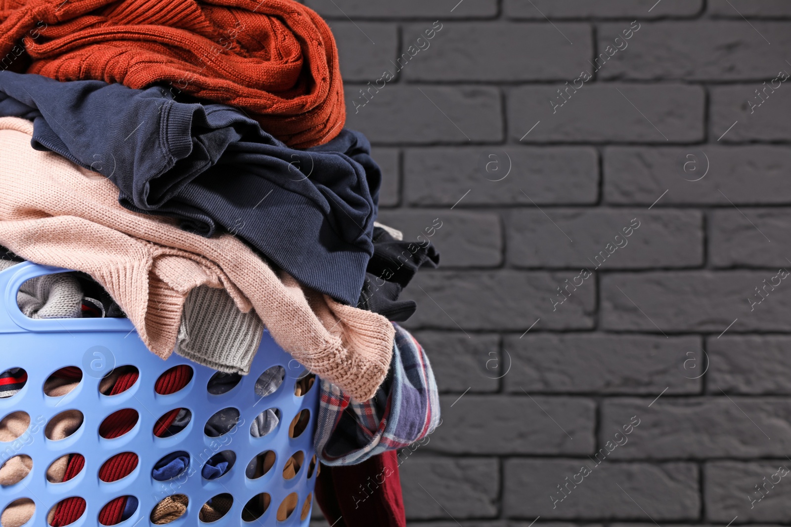 Photo of Laundry basket with clothes near black brick wall. Space for text