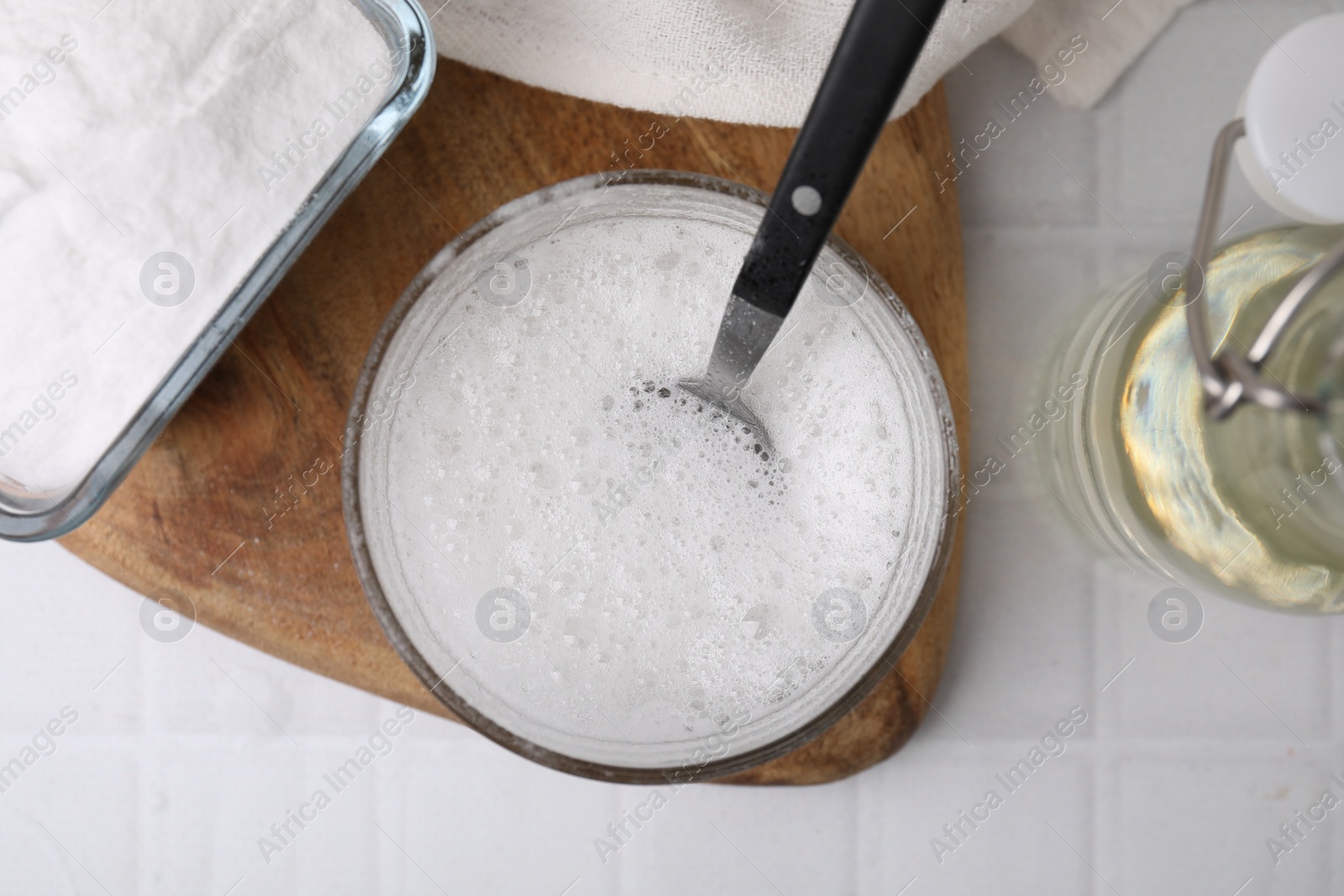 Photo of Chemical reaction of vinegar and baking soda in glass bowl on white tiled table, top view