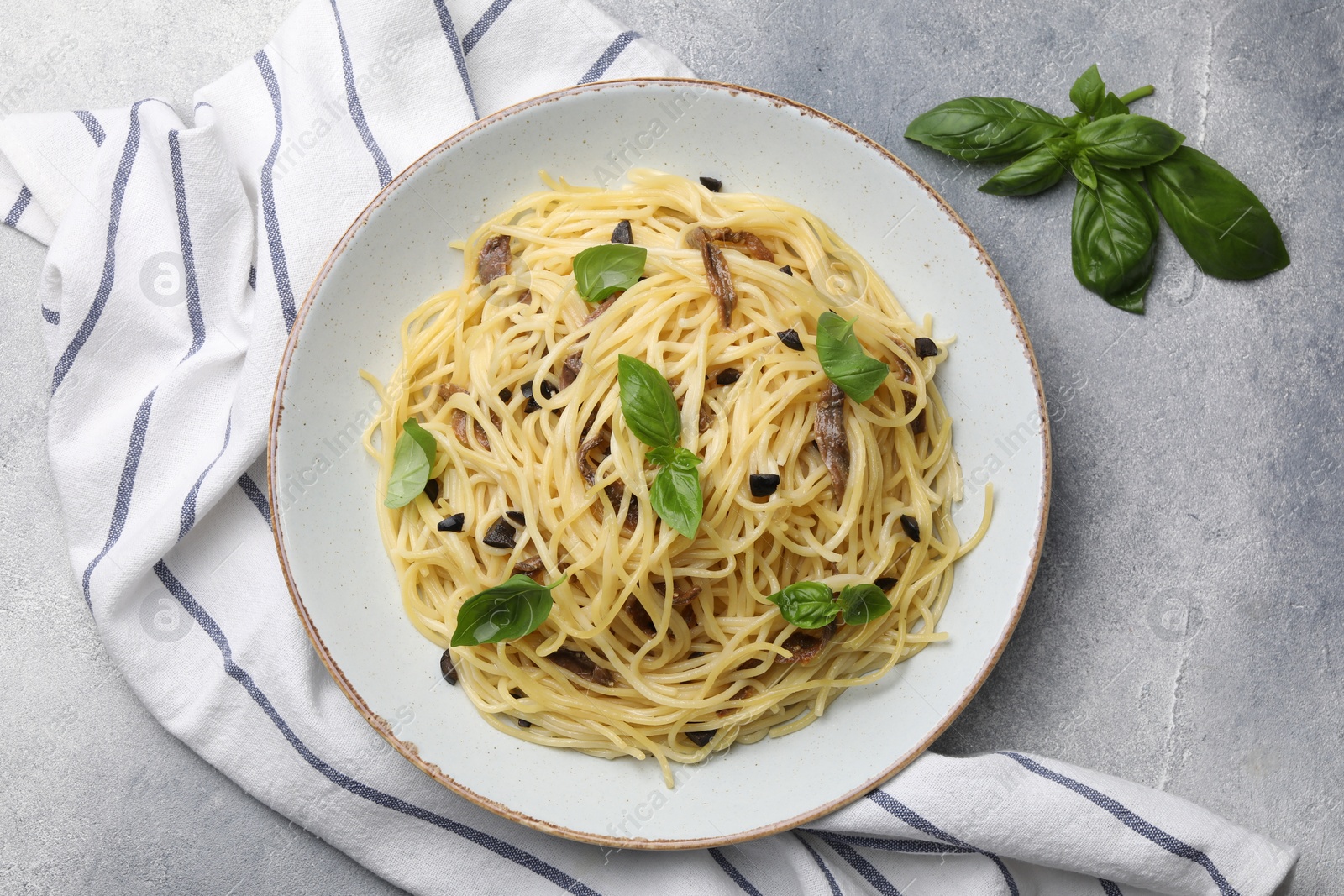 Photo of Delicious pasta with anchovies, olives and basil on light grey table, flat lay