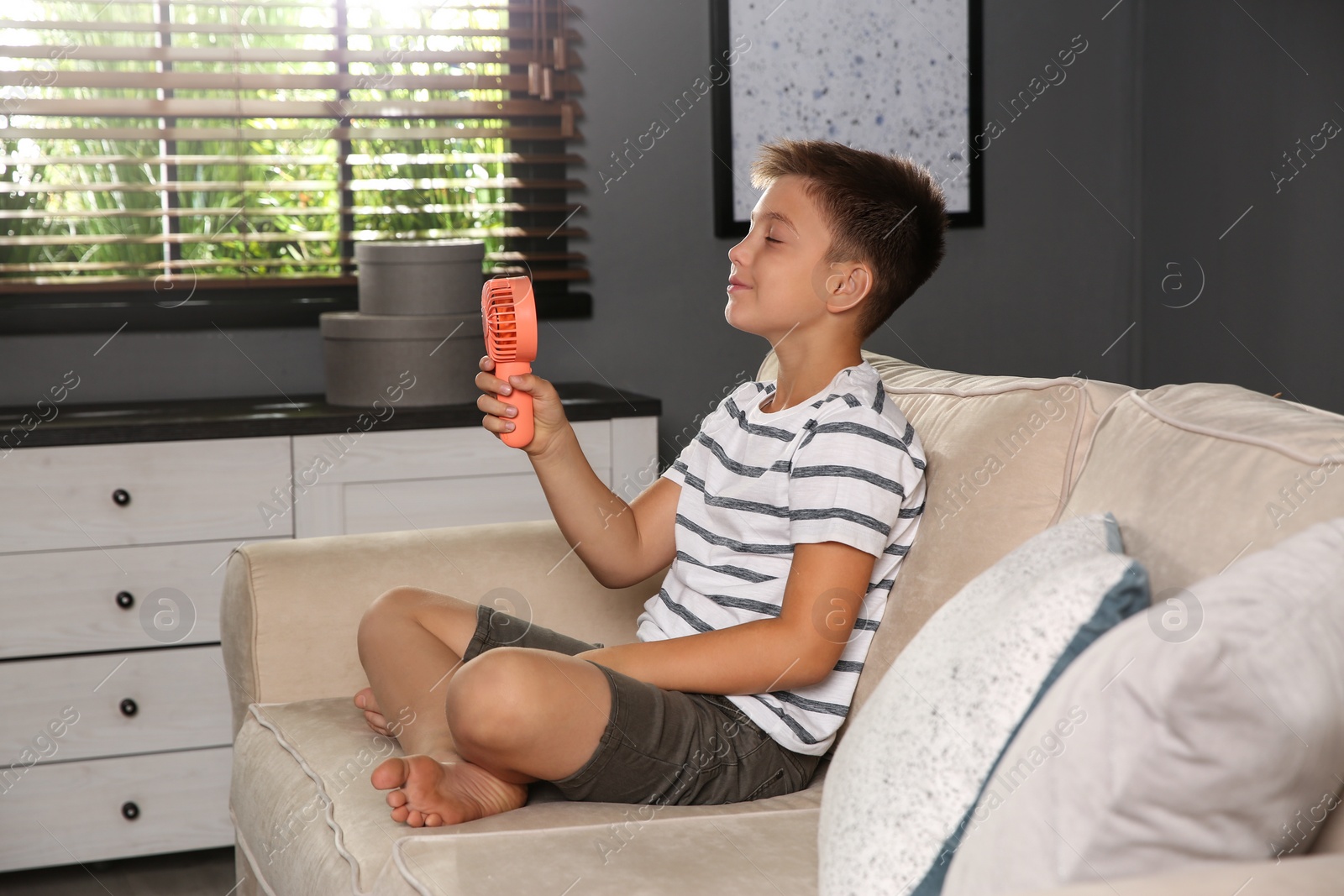 Photo of Little boy enjoying air flow from portable fan at home. Summer heat