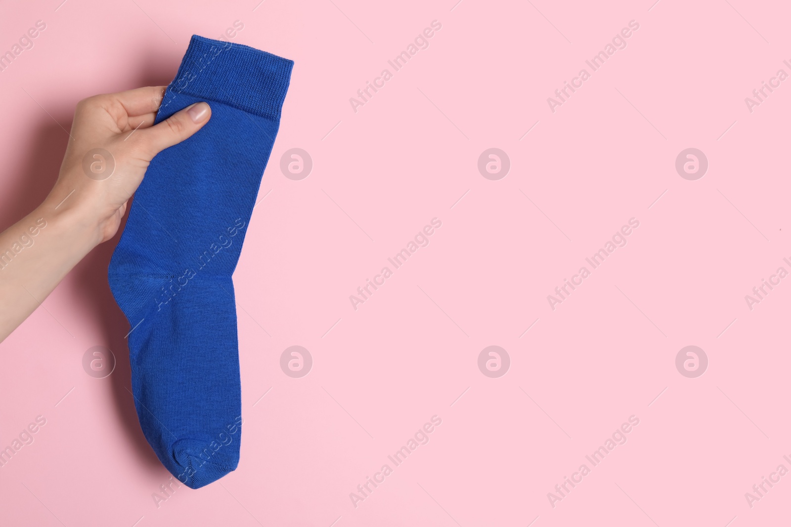 Photo of Woman holding blue sock on light pink background, closeup. Space for text