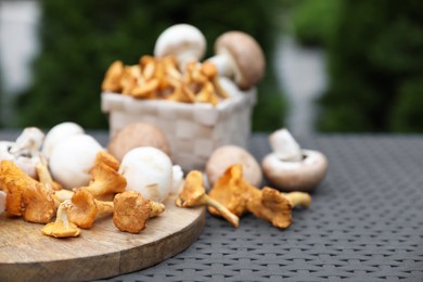 Photo of Different fresh mushrooms, board and basket on grey rattan table outdoors, space for text