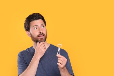 Photo of Handsome man with tongue cleaner on yellow background, space for text