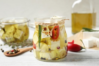 Jar with feta cheese marinated in oil on white wooden table. Pickled food