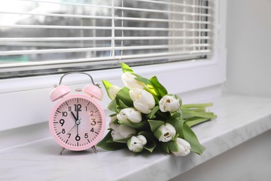 Photo of Pink alarm clock and wonderful tulips on window sill indoors. Spring atmosphere