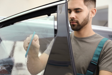 Photo of Worker washing tinted car window in workshop, focus on hand