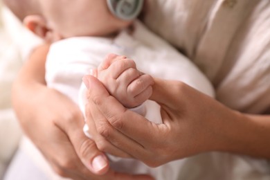 Mother holding newborn baby indoors, focus on hands