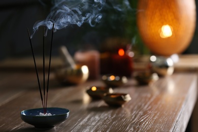 Photo of Incense sticks smoldering on wooden table in room. Space for text