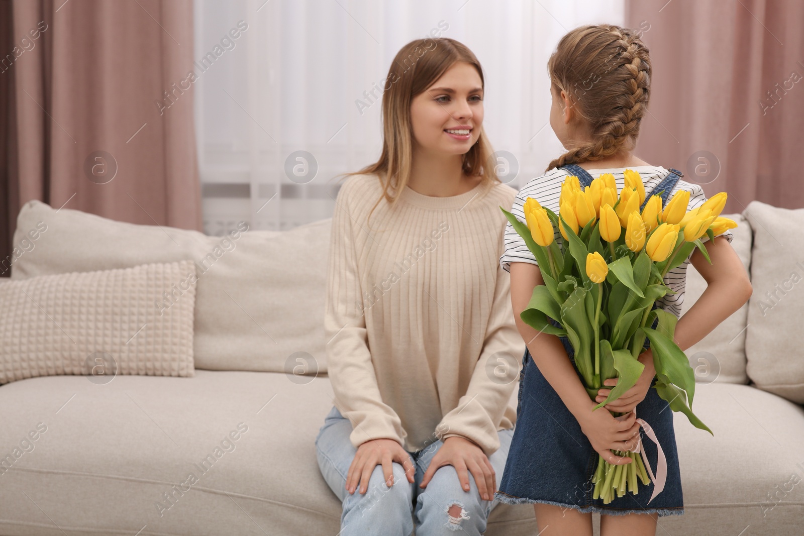 Photo of Little daughter congratulating mom with bouquet of yellow tulips at home. Happy Mother's Day