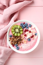 Tasty smoothie bowl with fresh kiwi fruit, berries and granola on pink wooden table, top view